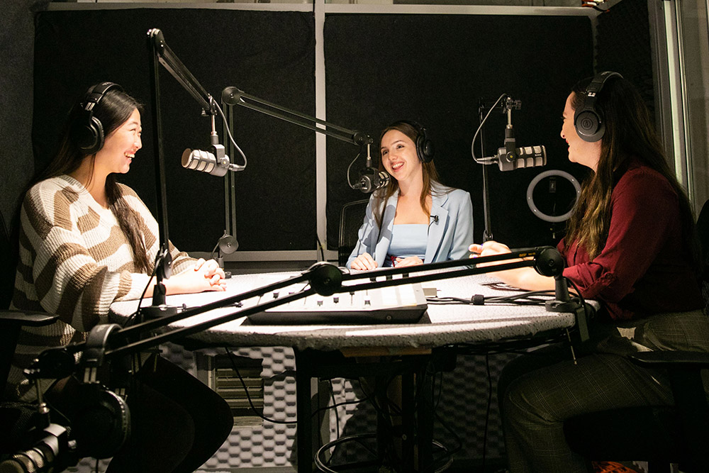 Three female students in front of microphones at the radio station
