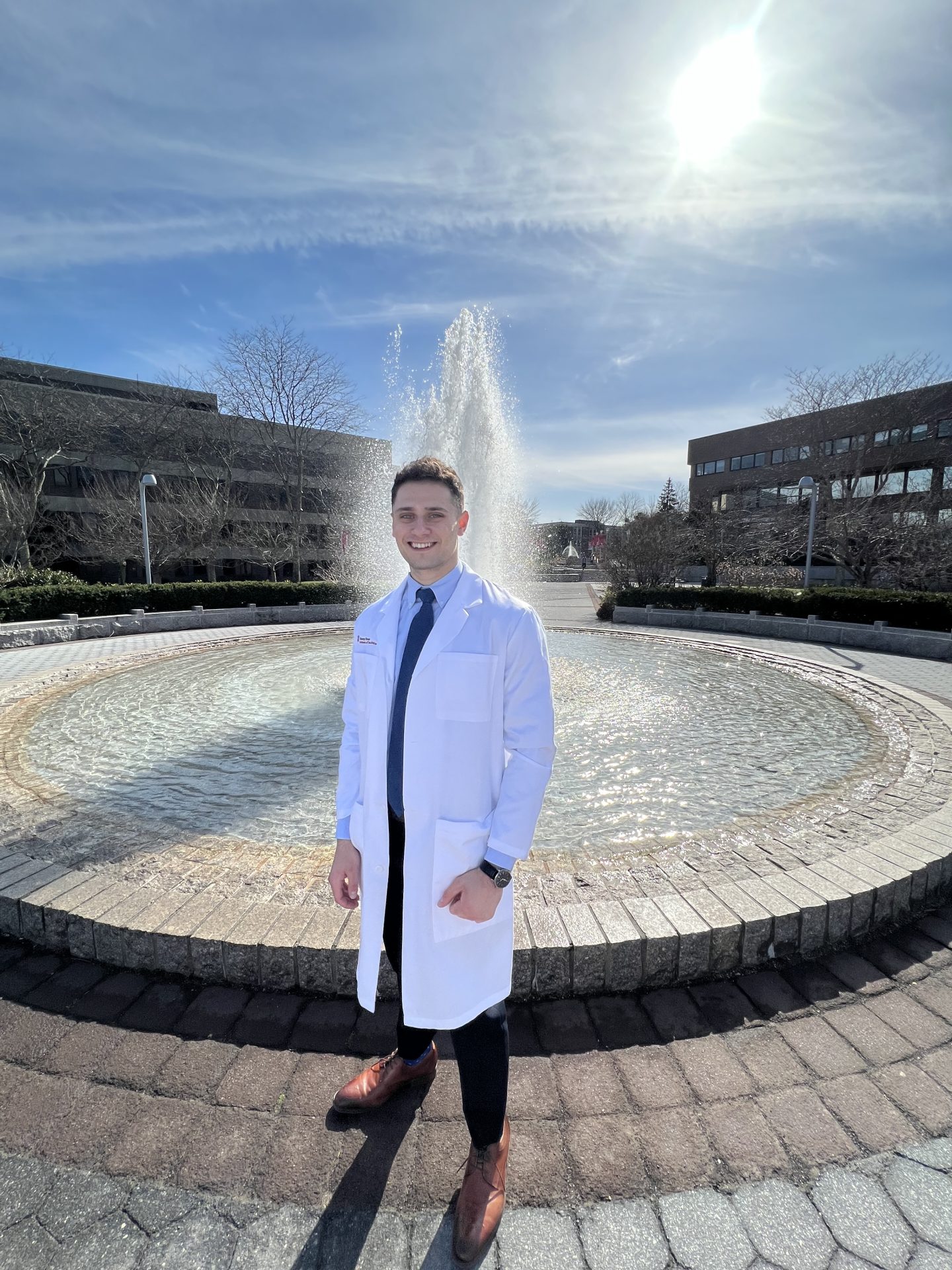 Axelrod stands in front of the Administration fountain on campus, wearing a white coat.