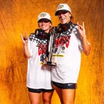 Two women in championship shirts post with a trophy.