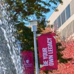 Water fountain on the left and fall trees on the right with a Be Your Own Legacy sign