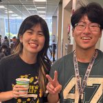 Two students, one giving the peace sign, the other holding a cup of coffee