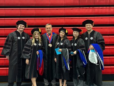 Zahraa Krayem Stuart surrounded by fellow graduaes and her professor
